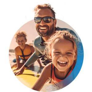 Vater, Tochter und Sohn mit Schwimmwesten auf Surfboard am Strand lachen in die Kamera.